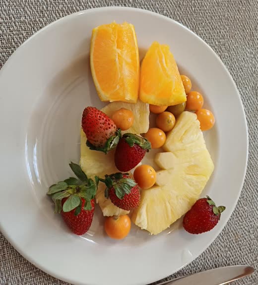 A plate of fresh fruit including pineapple, orange and strawberries